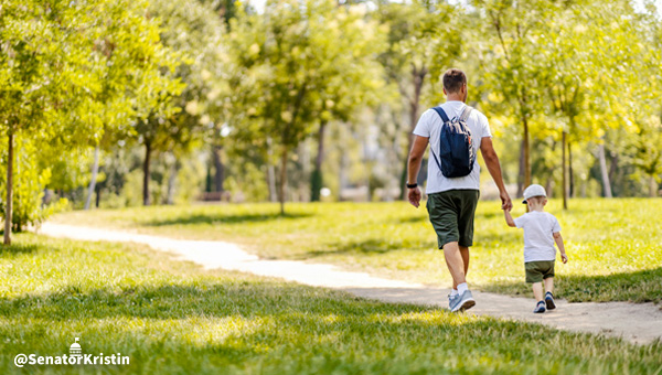 A father and young son walking through a park, holding hands.