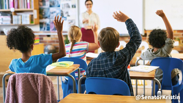 Children raising their hands in a classroom.