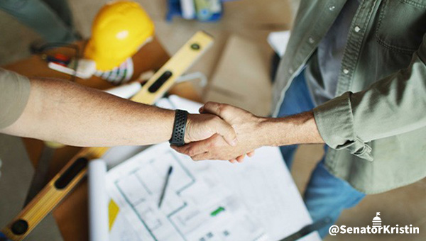 Men shaking hands over building blueprints.